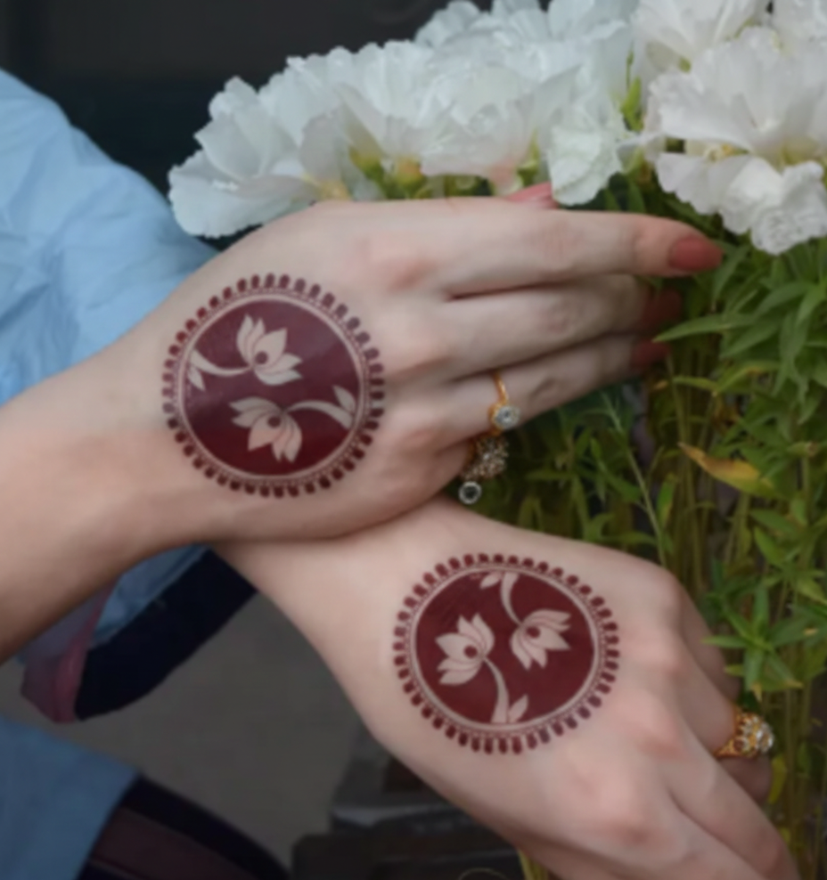 Hands with floral henna designs held against a background of white flowers.